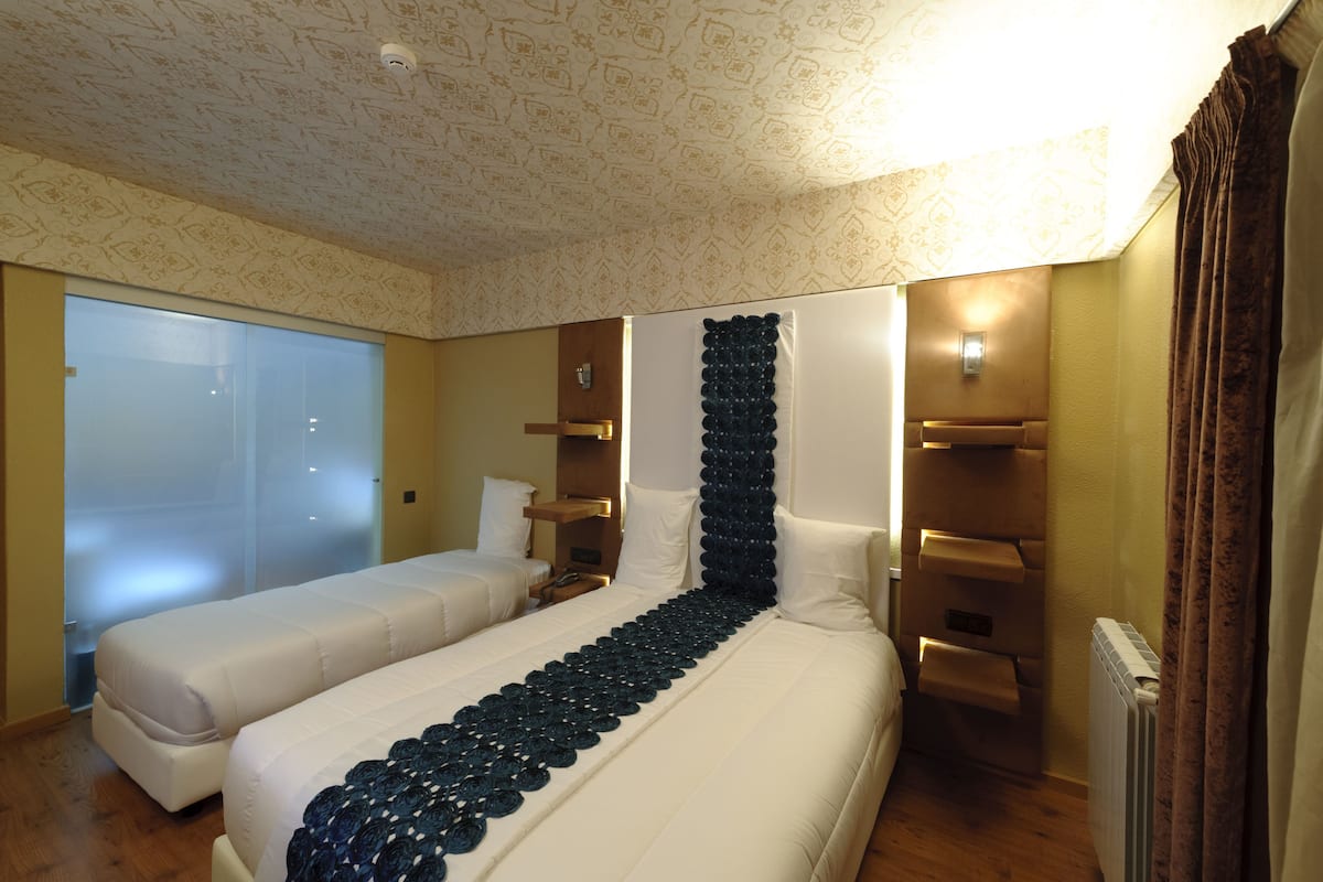 A hotel room with a large bed, a smaller bed, a wall-mounted heater, and a glass partition.