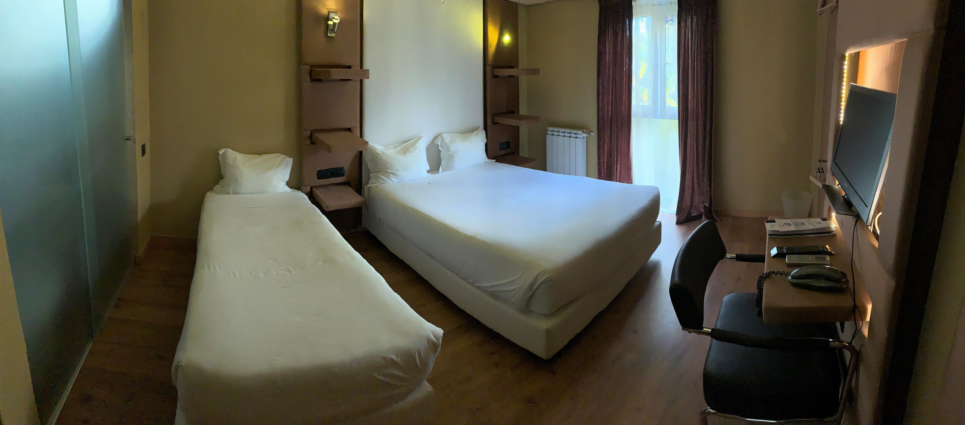 Una habitación de hotel con dos camas individuales, un escritorio con silla, televisor y radiador.