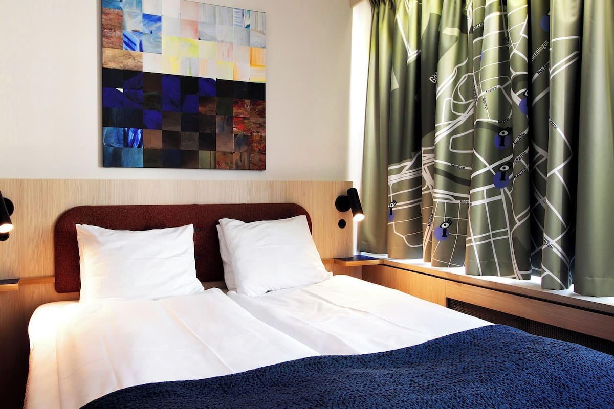 Een hotelkamer met een bed, twee nachtkastjes, een kunstwerk aan de muur en gordijnen.