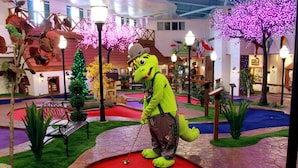 A mascot in a golf-themed area with a putting green, benches, and decorative trees. - Bavarian Inn of Frankenmuth (Frankenmuth)
