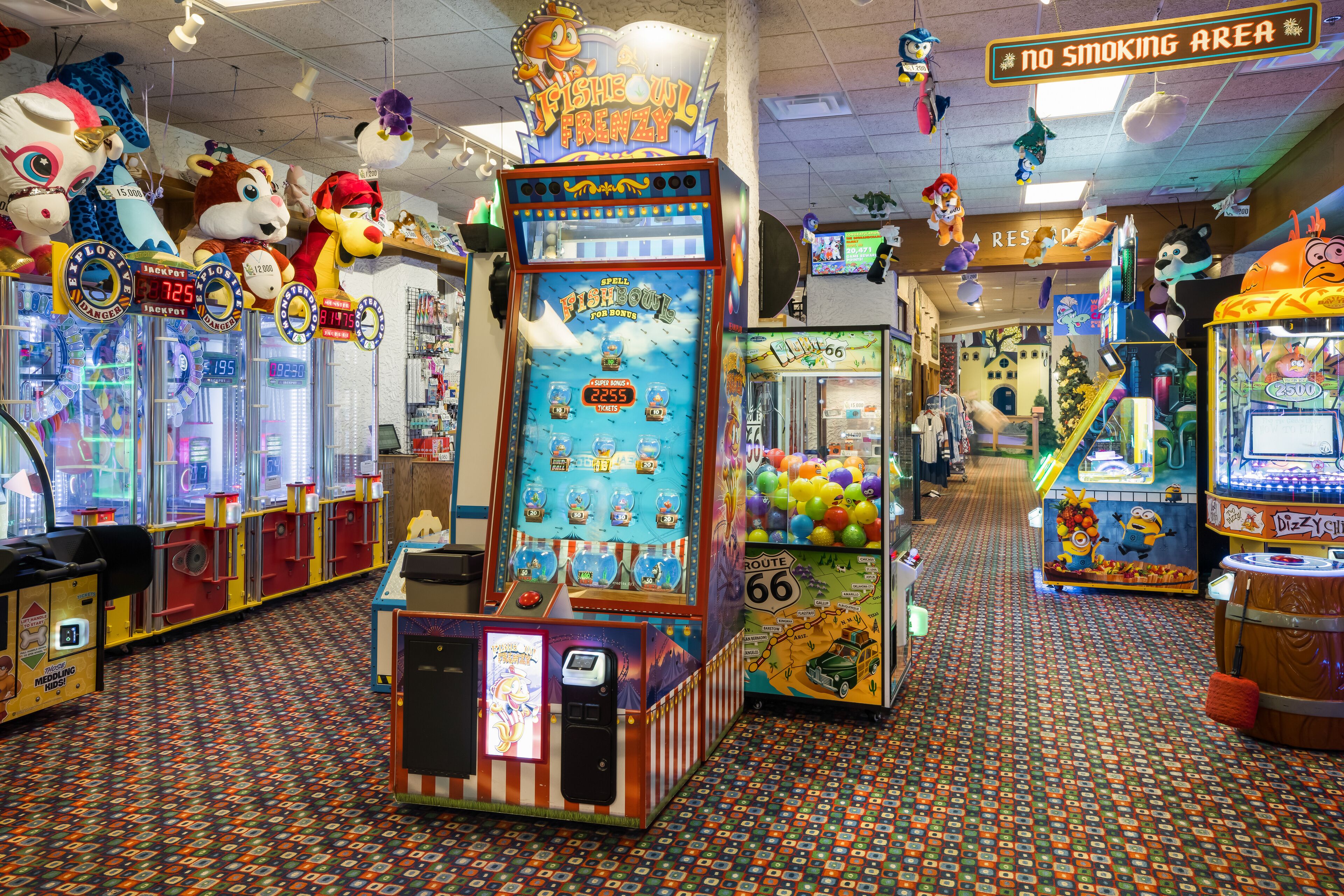 A brightly lit arcade with various gaming machines, including a 'Fish Bowl Frenzy' game, and a 'No Smoking Area' sign.