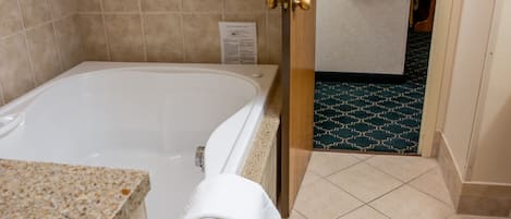 A bathroom with a bathtub, a towel on the edge, a door leading to another room, and a patterned floor.