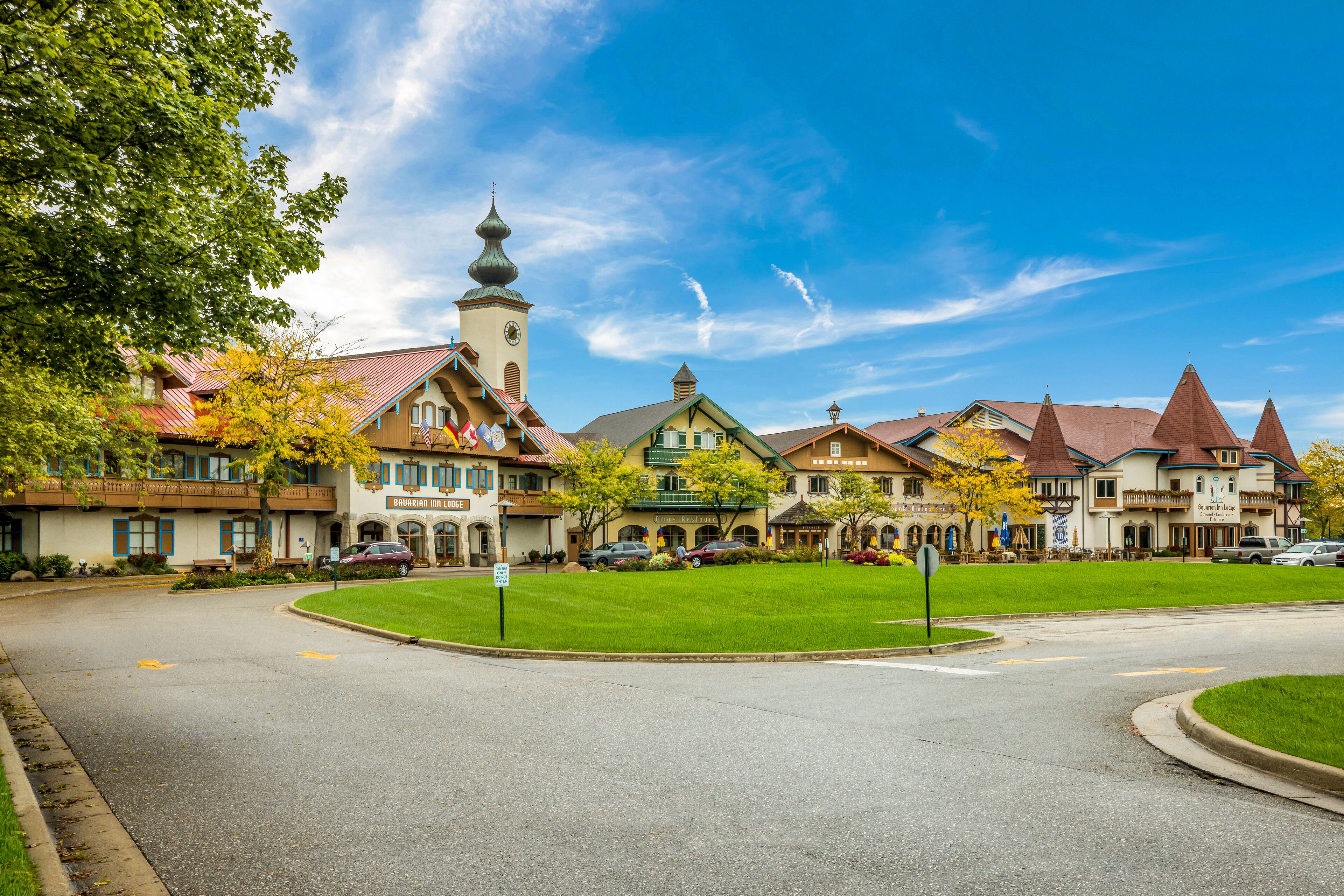 A historic building with a clock tower, surrounded by a well-maintained lawn and parked cars.