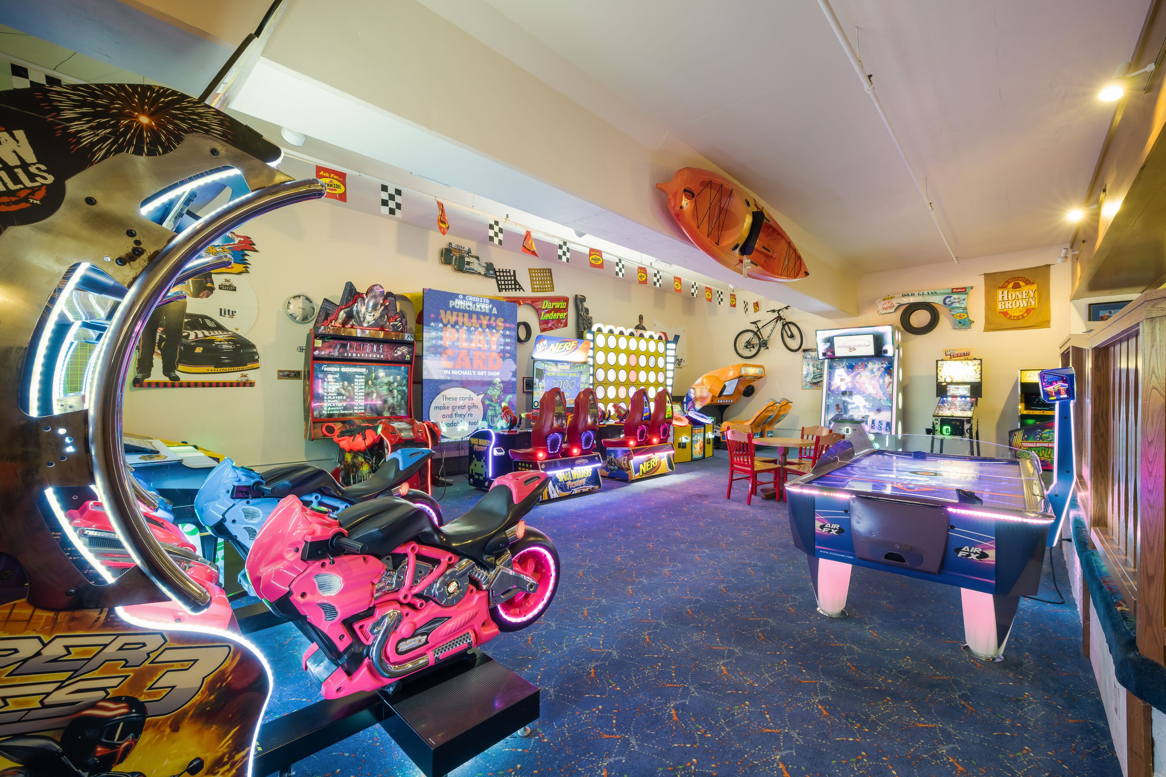 A room with arcade games, a ping pong table, and a motorcycle.