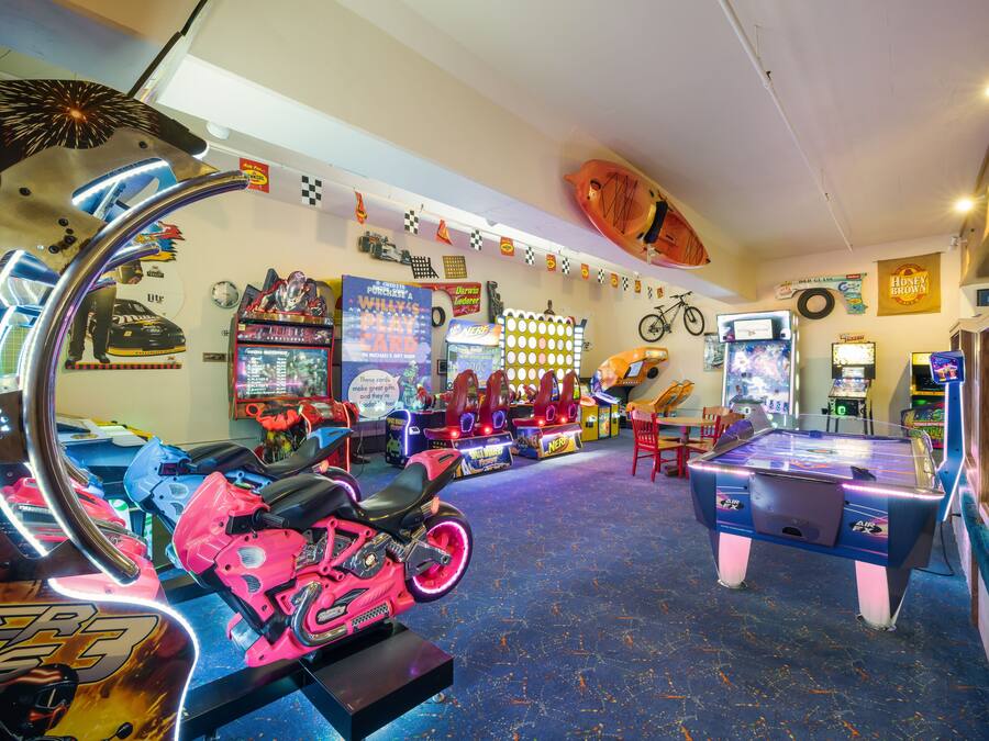 A room with arcade games, a ping pong table, and a motorcycle.