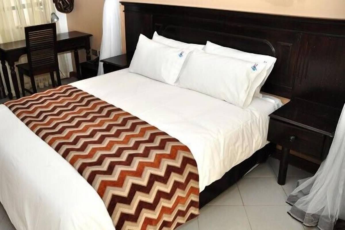 A neatly made bed with a patterned bedspread, a dark headboard, and a bedside table with a lamp.
