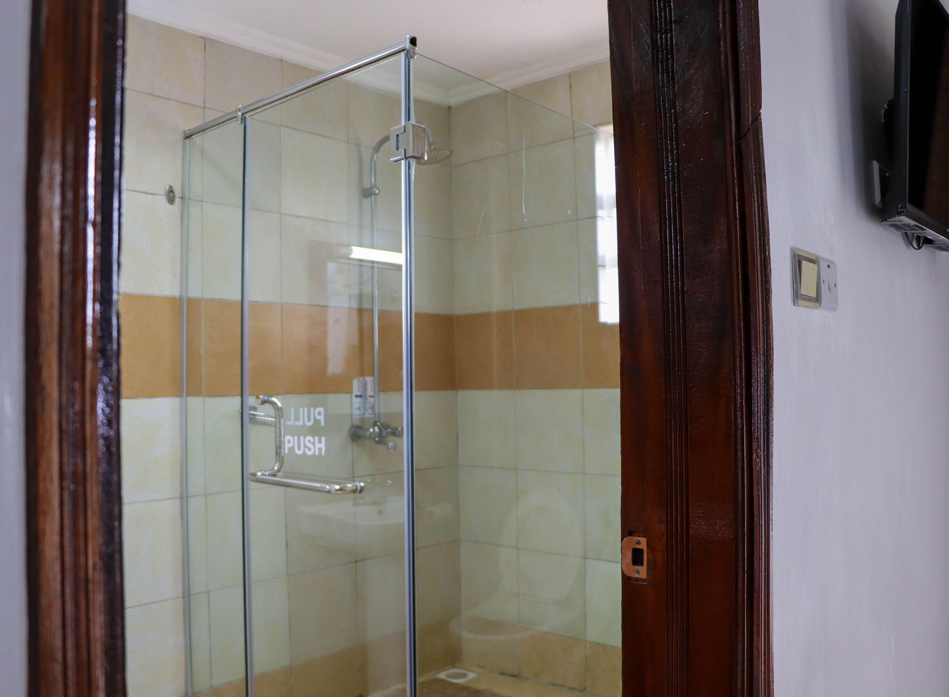 A glass-enclosed shower with a push button and a handrail.