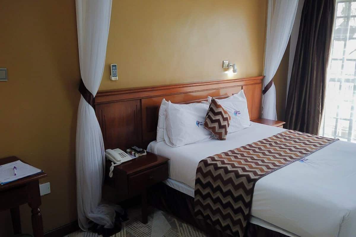 A hotel room with a bed, a nightstand, a telephone, and a window with curtains.