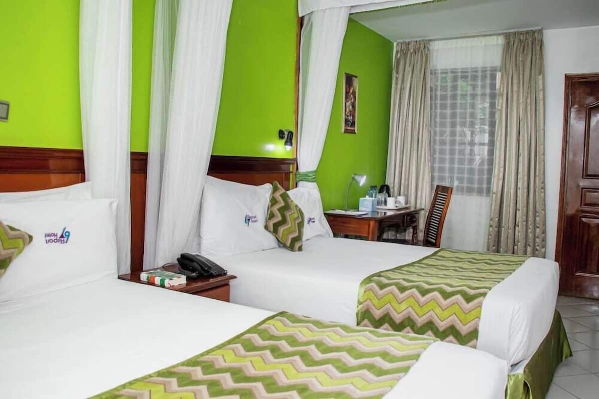 A hotel room with two beds, a desk, a chair, a nightstand, a lamp, and a window with curtains.