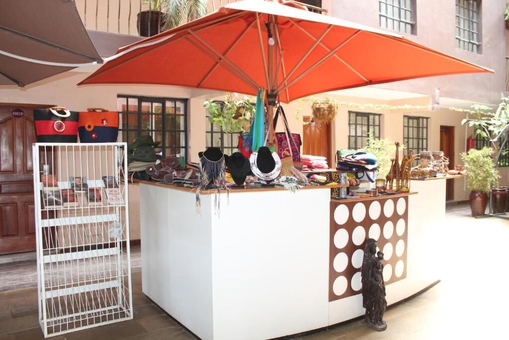 A small outdoor kiosk with a white counter and a large orange umbrella. There are various bags and accessories displayed on the counter.