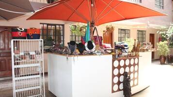 A small outdoor kiosk with a white counter and a large orange umbrella. There are various bags and accessories displayed on the counter.