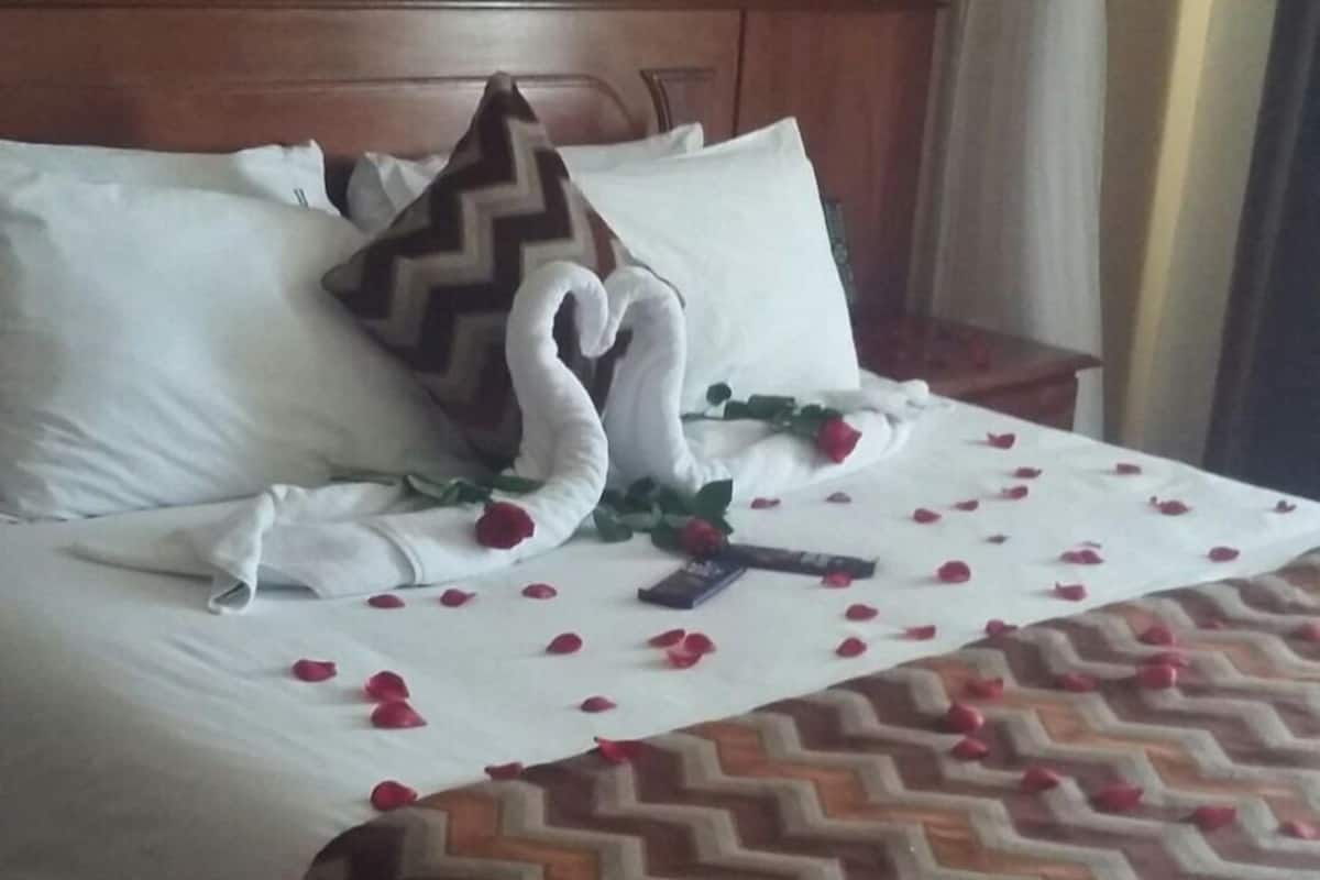 A hotel room with a bed, a wooden headboard, a patterned bedspread, and a white pillow with a logo.