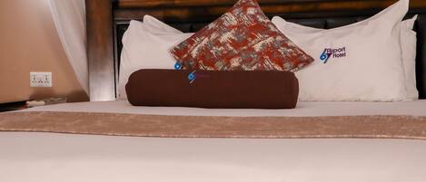 Un lit avec une literie blanche, un oreiller marron et un oreiller à motifs rouges.