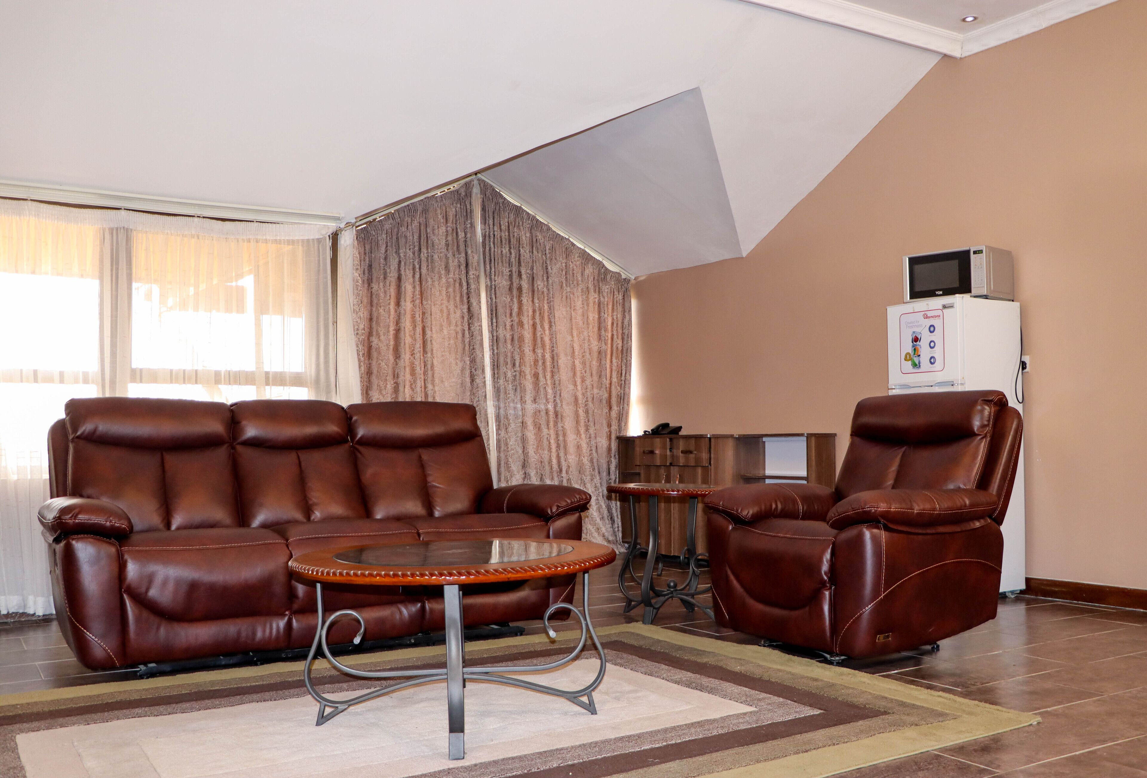Una sala de estar con un sofá de cuero marrón, una mesa redonda de centro y un sillón reclinable. Hay un microondas sobre una pequeña mesa junto a la pared.