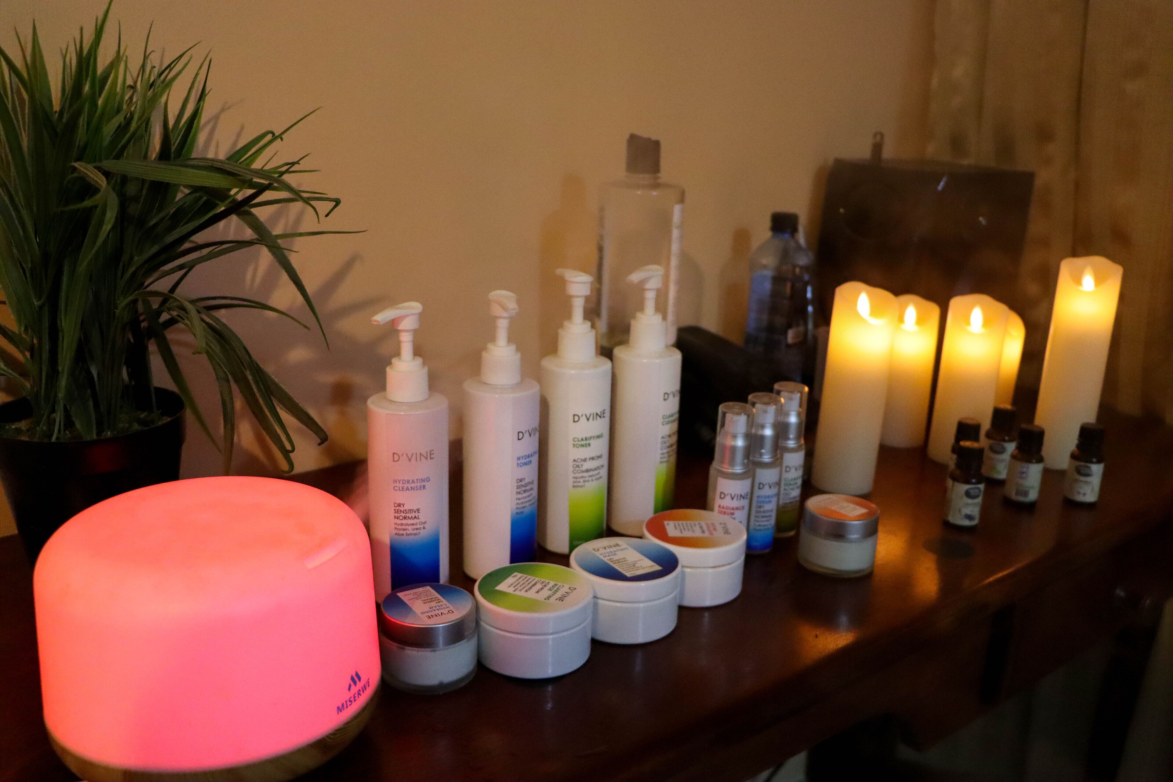 A table with various skincare products, candles, and a diffuser.
