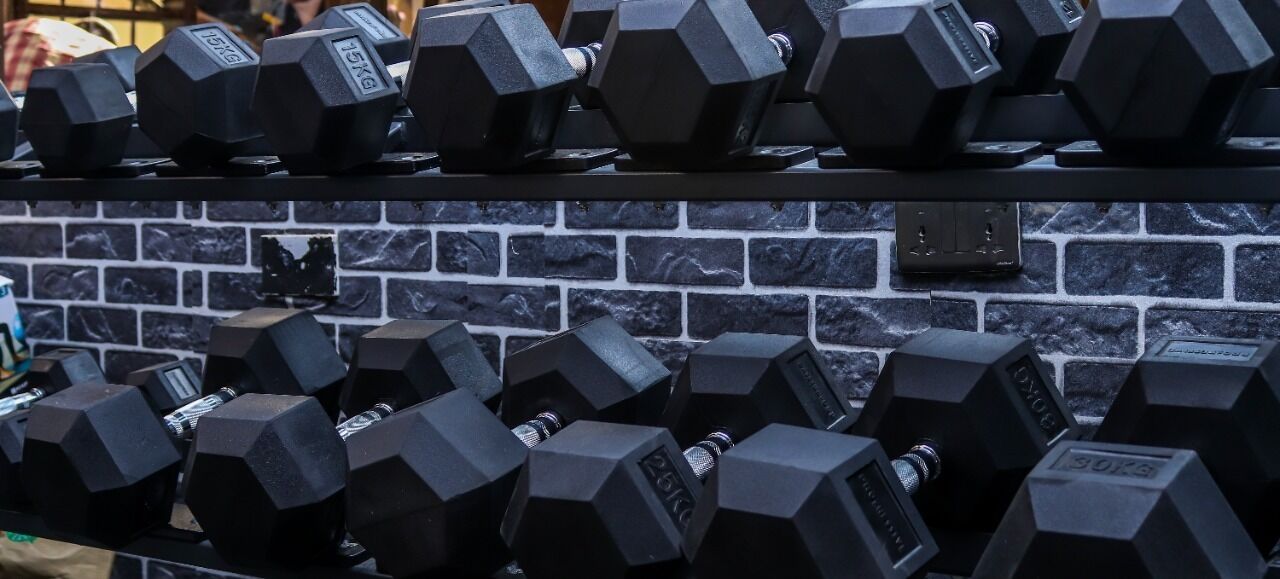 A rack of black dumbbells with weight markings, against a brick wall background.