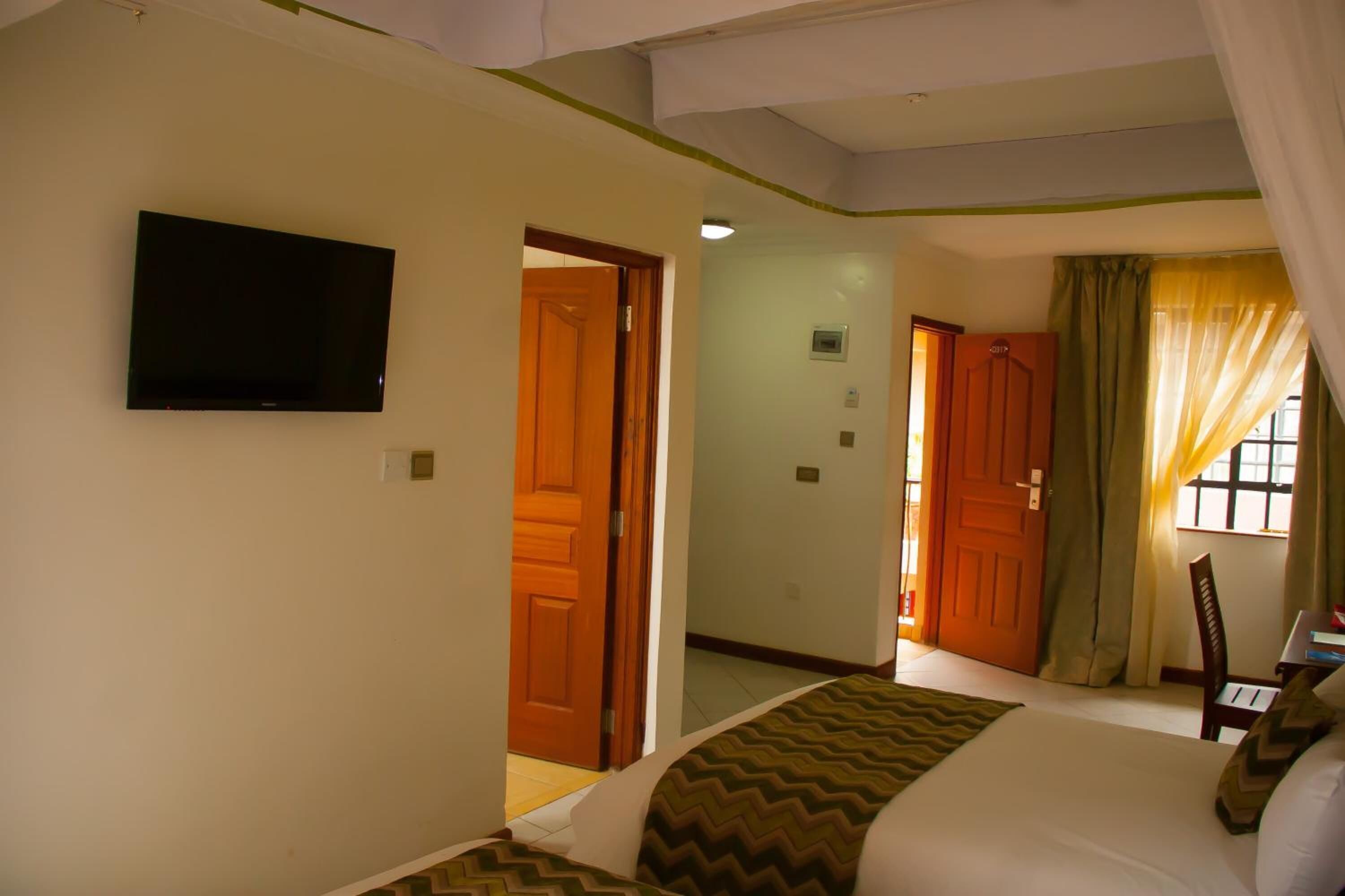 Une chambre d’hôtel avec un lit, un téléviseur fixé au mur et une porte donnant sur une autre pièce.