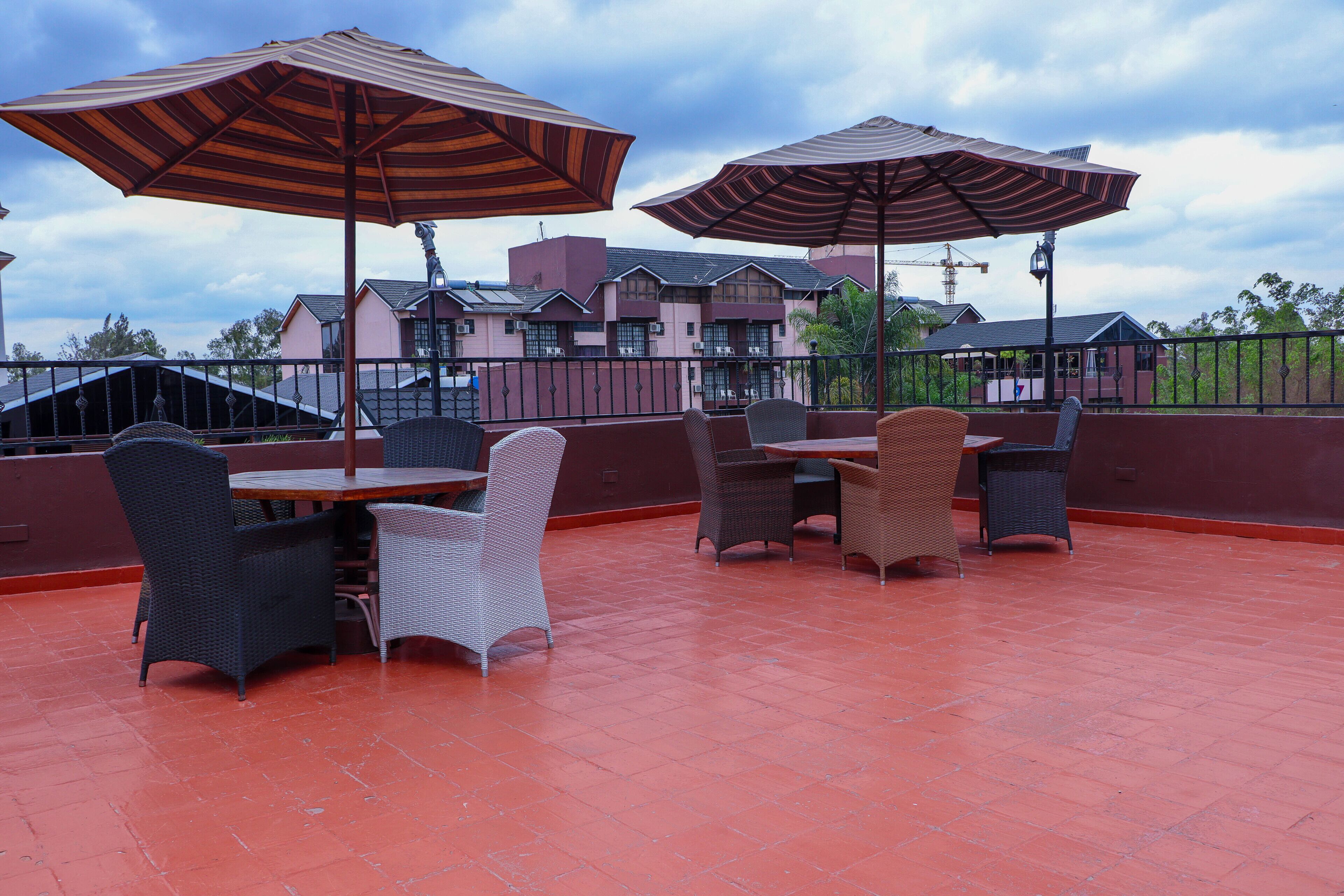 Un patio exterior con mobiliario de mimbre y grandes sombrillas, con vista a una zona residencial con casas y una grúa.