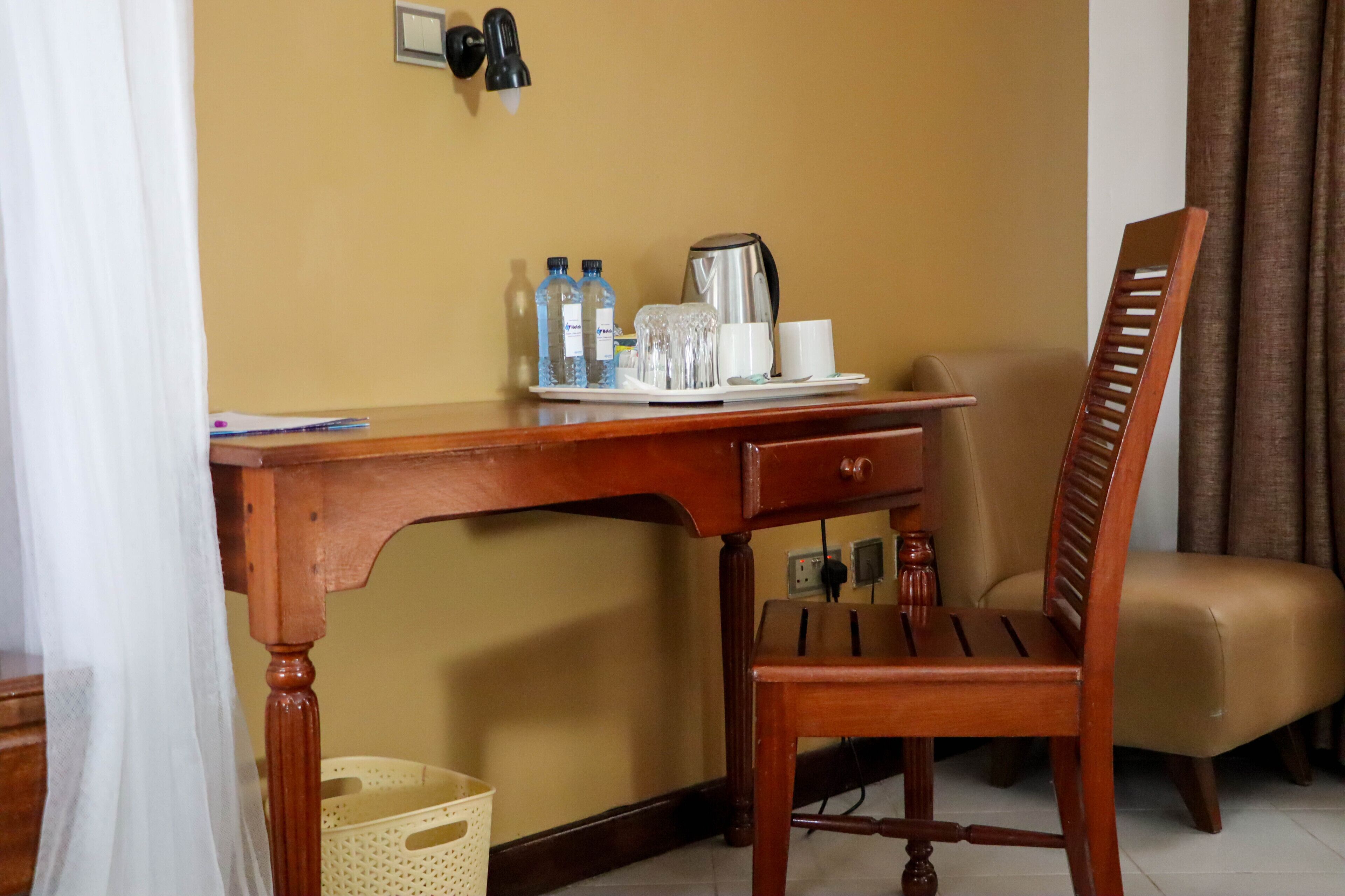 A wooden desk with a chair, a coffee maker, and a tray with bottles and glasses.