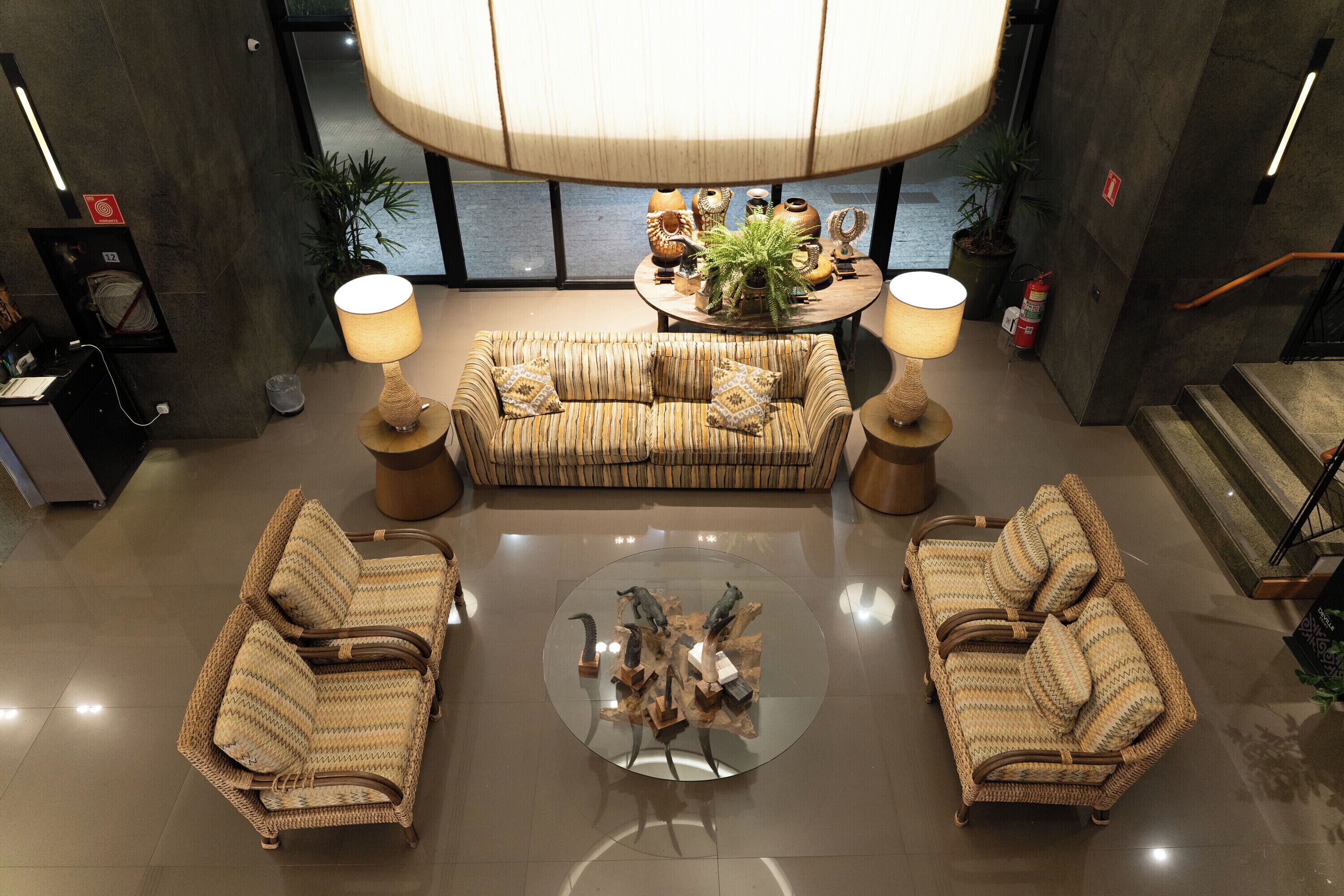 A spacious lobby with a large sofa, two armchairs, a round coffee table, and a central plant display.