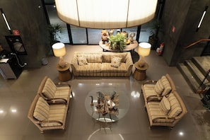 A spacious lobby with a large sofa, two armchairs, a round coffee table, and a central plant display.