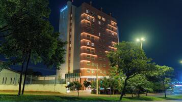A multi-story hotel with a prominent sign at the top, a well-lit entrance, and a parking area in front.