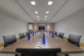 A conference room with a long table, black chairs, blue water bottles, and a projector screen. - Hotel Deville Prime Campo Grande (Campo Grande)