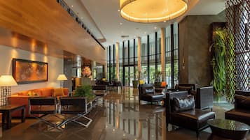 A modern lobby with a wooden reception desk, seating area, and large windows.