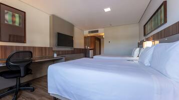 Habitación de hotel con dos camas, un escritorio con silla, televisión y obras de arte en las paredes.
