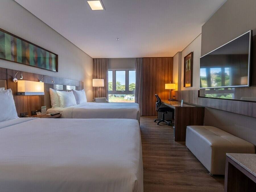 A hotel room with two beds, a desk, a chair, a TV, and a window with a view.