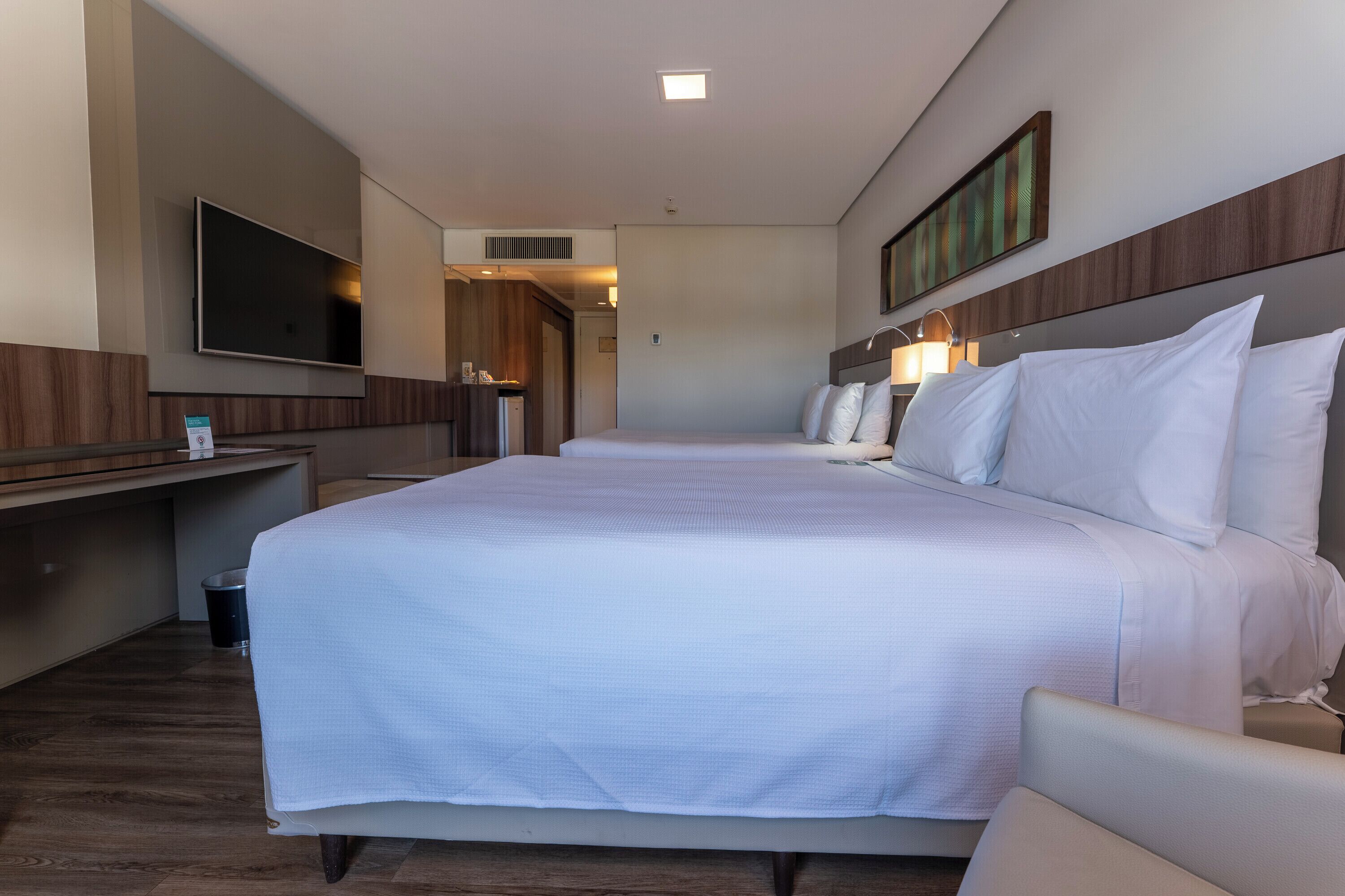 A hotel room with a large bed, a desk, a flat-screen TV, and a mirror.