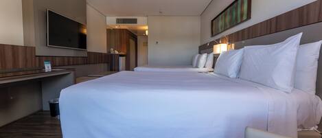 A hotel room with a large bed, a desk, a flat-screen TV, and a mirror.