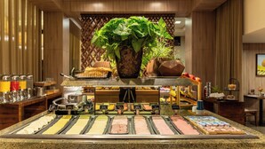 Zona de buffet con diversas opciones de comida, una estación de café y una planta decorativa.