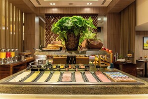 Zona de buffet con diversas opciones de comida, una estación de café y una planta decorativa.