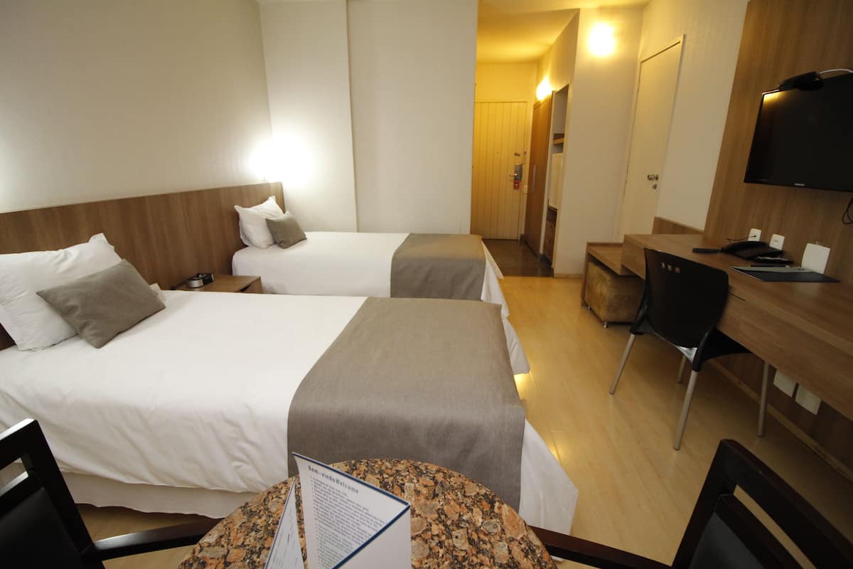 A hotel room with two beds, a desk, a chair, and a television.