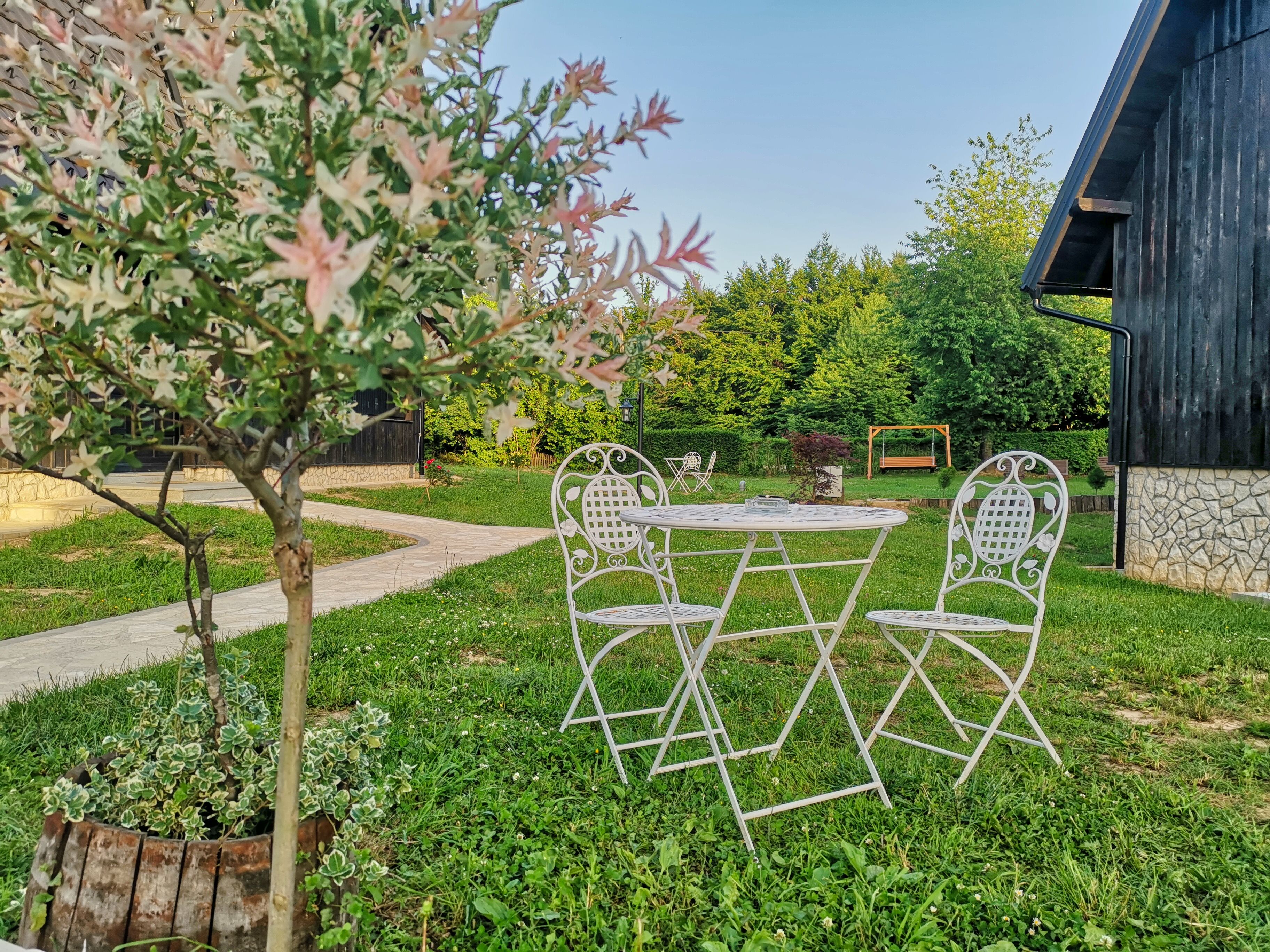A garden with a white metal table and chairs, surrounded by greenery and a stone wall.