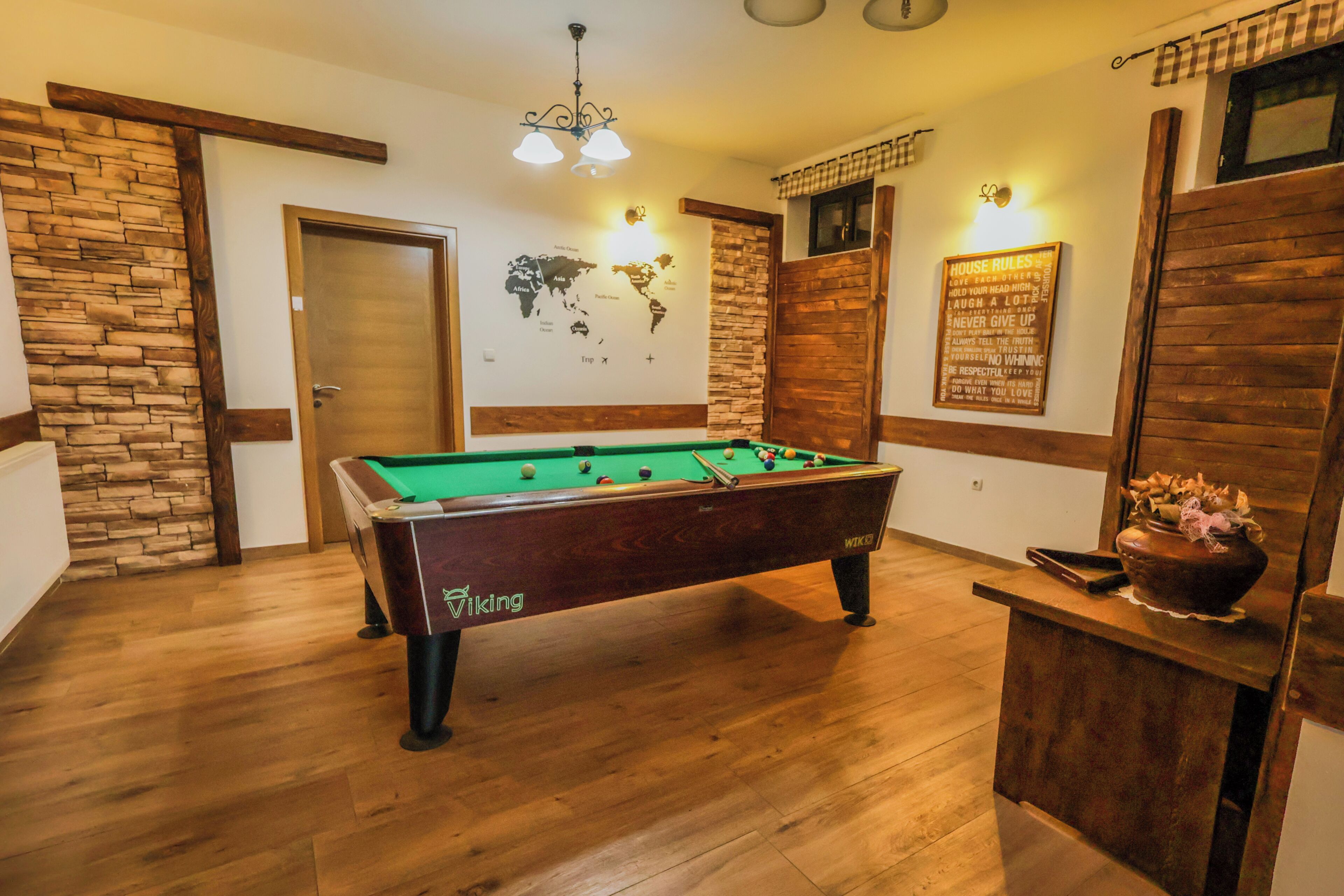 A pool table in a room with wooden flooring, a world map on the wall, and a 'House Rules' sign.