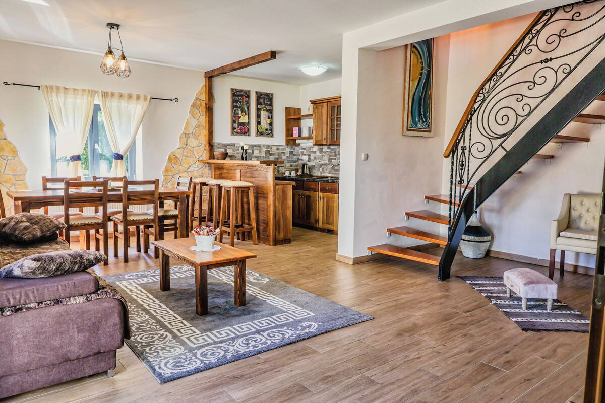 A modern living room with a dining area, kitchen, and staircase.