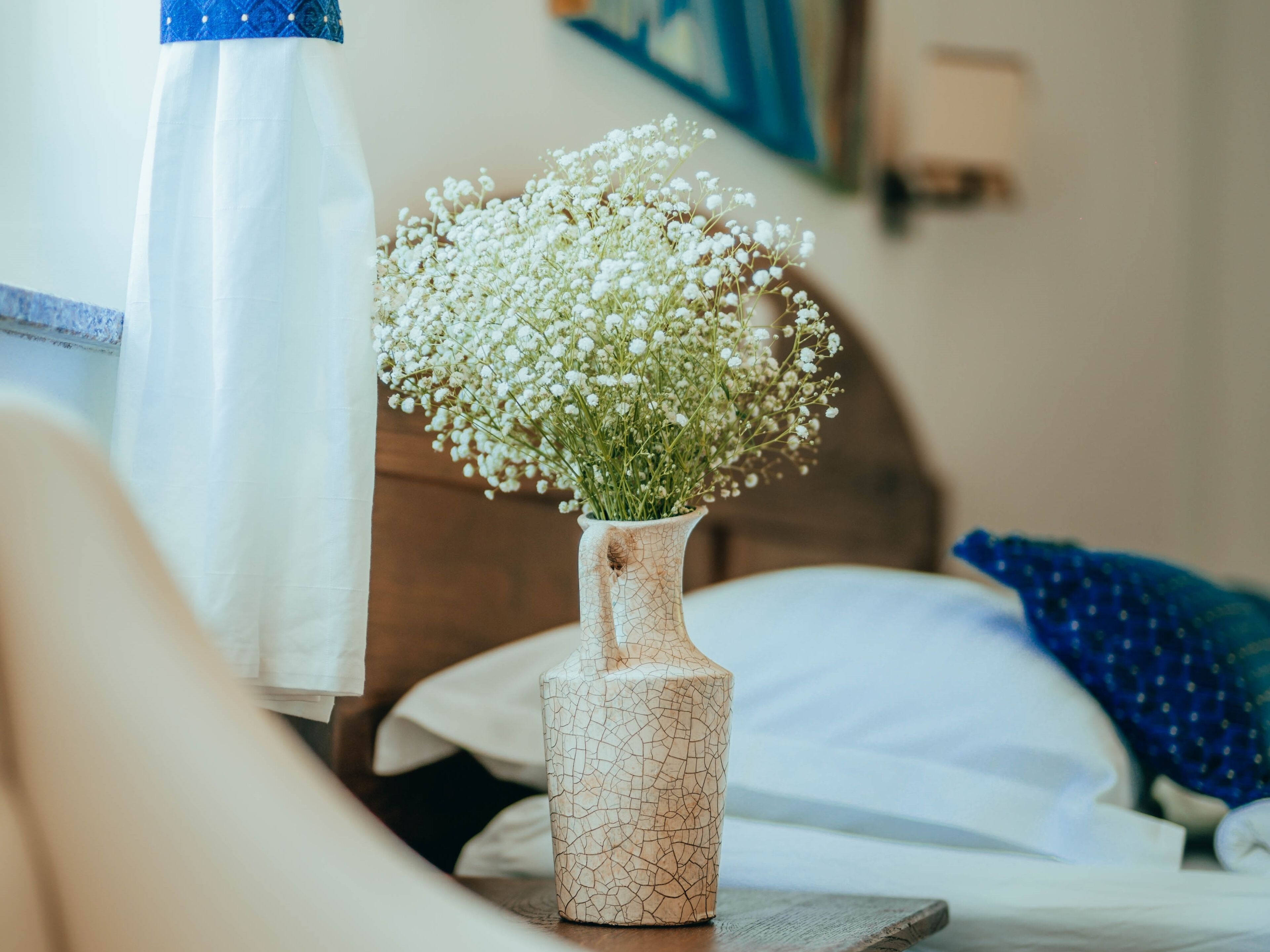 A vase with white flowers on a bedside table in a hotel room.