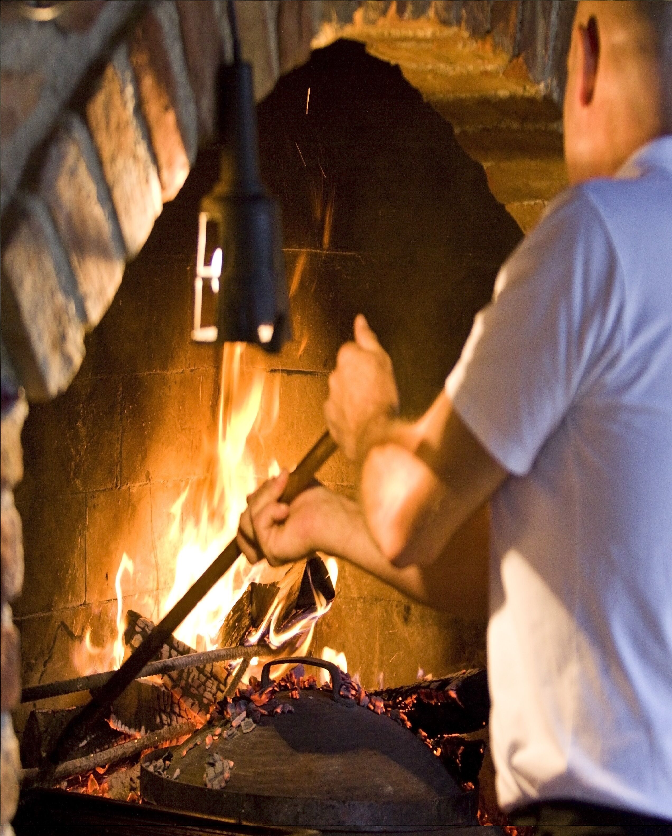 A person using a tool to manage a fire in a brick oven.
