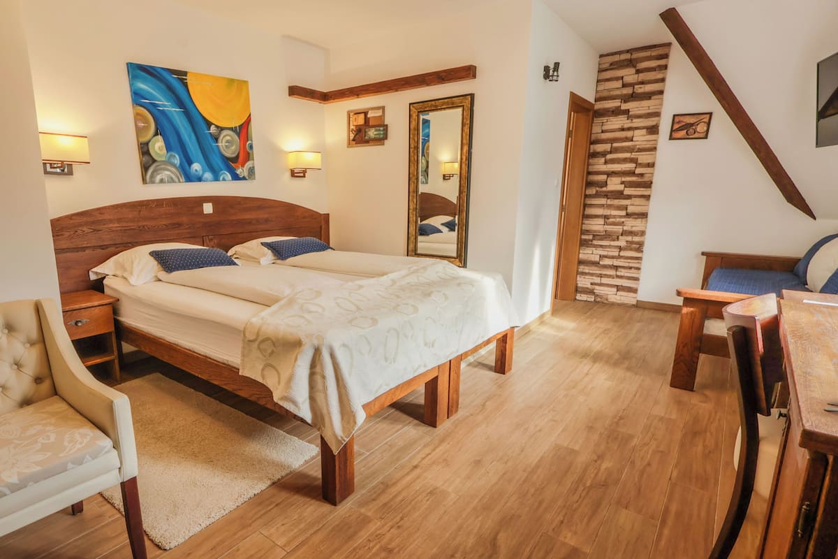A bedroom with a wooden bed, bedside tables, a chair, a desk, a mirror, and a painting on the wall.