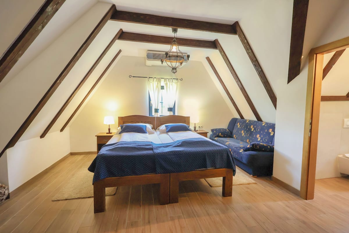 A bedroom with a wooden bed, a sofa, a chandelier, and a window with curtains.