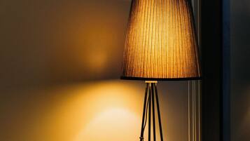 A wicker chair with a black cushion, a floor lamp with a ribbed shade, and a wall-mounted light fixture.