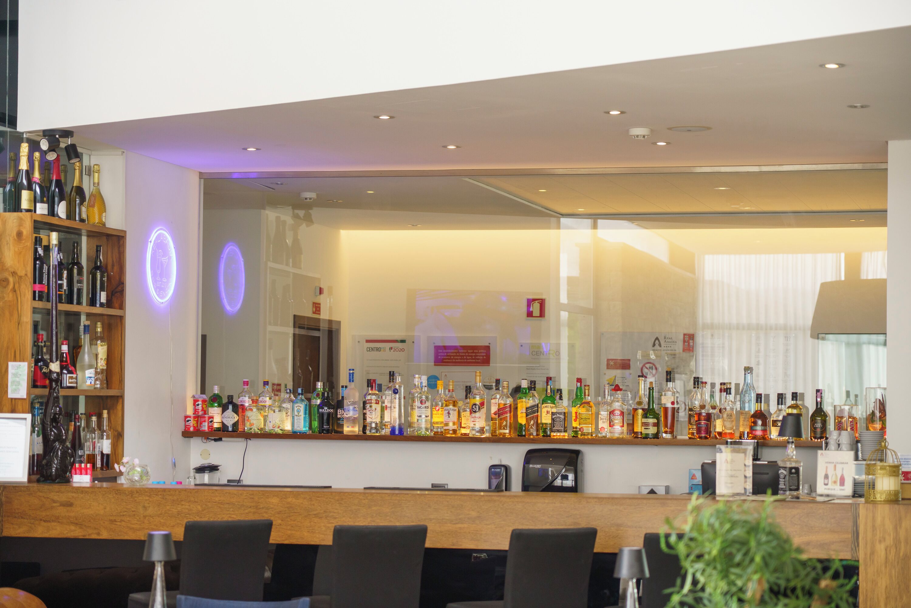 A bar area with a variety of liquor bottles, a wooden counter, and several chairs.