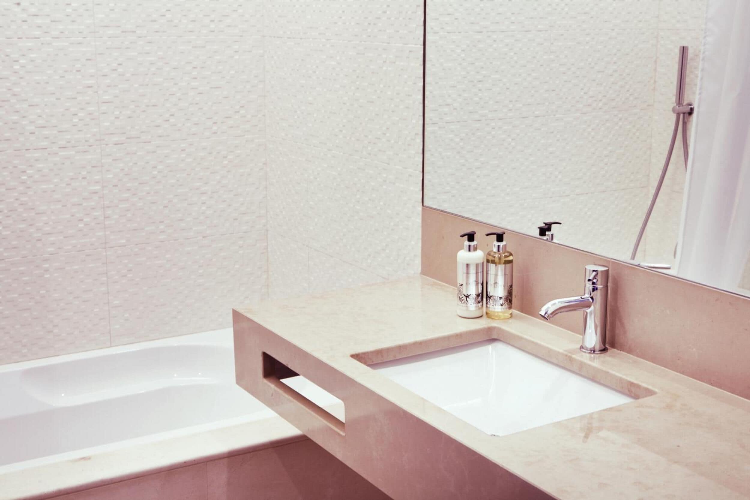 Ein Badezimmer mit einer weißen Badewanne, einem beige gefärbten Waschtisch mit zwei Becken und einem großen Spiegel.