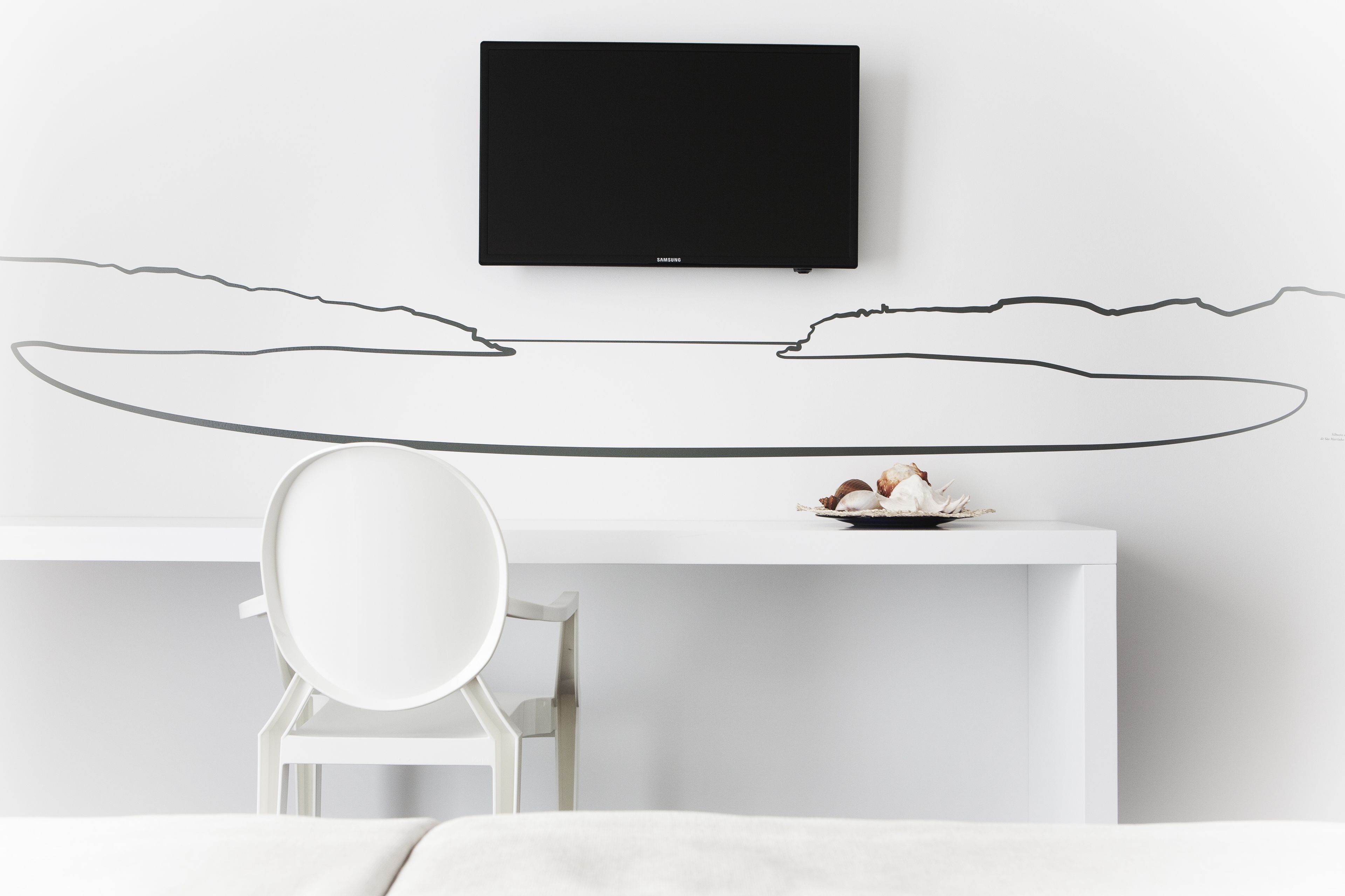 Una habitación moderna con un escritorio blanco, un televisor de pantalla plana en la pared y un dibujo sencillo de una playa.