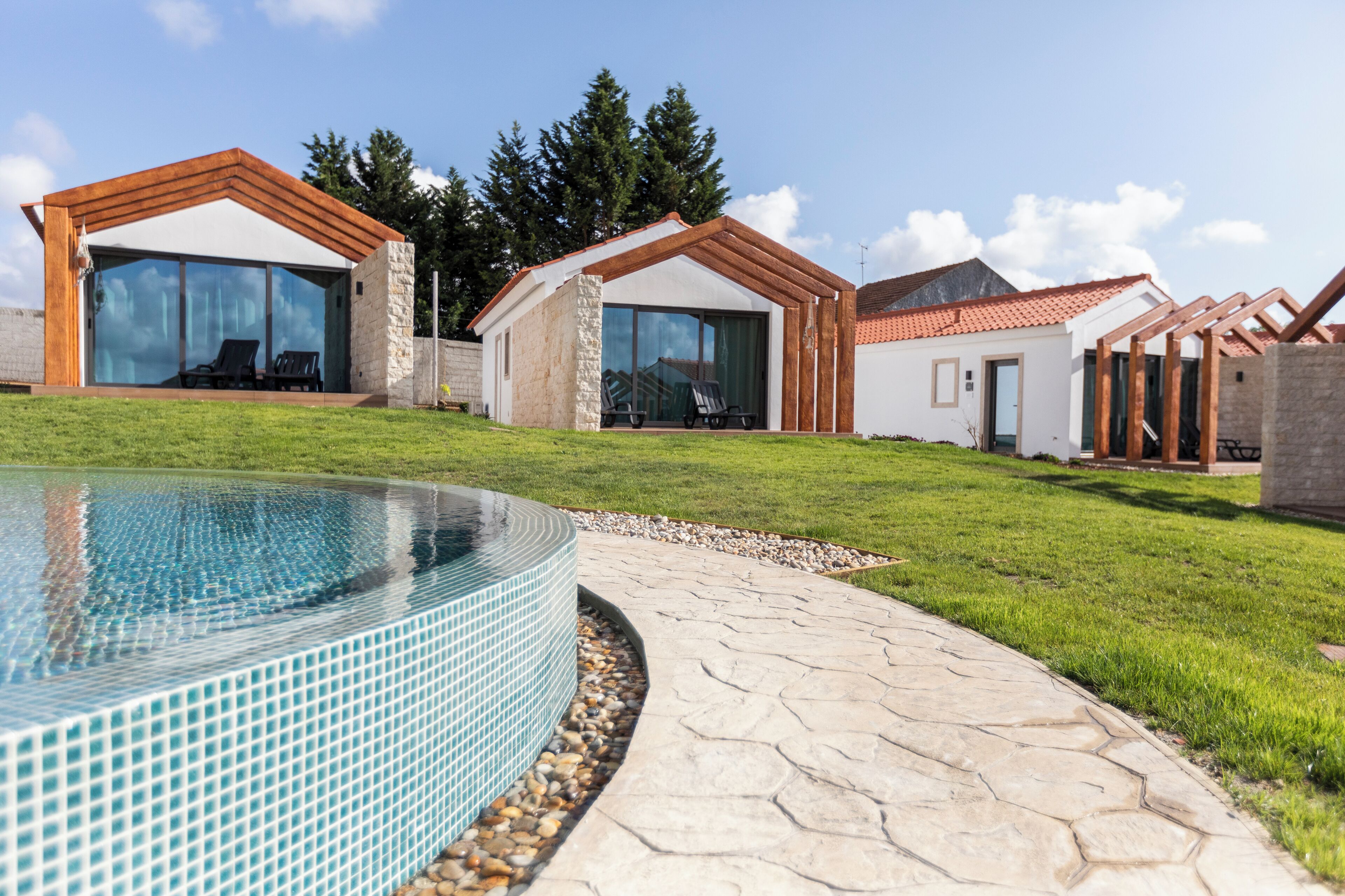 Un área de piscina moderna con borde de azulejos, un sendero de piedra y un césped.
