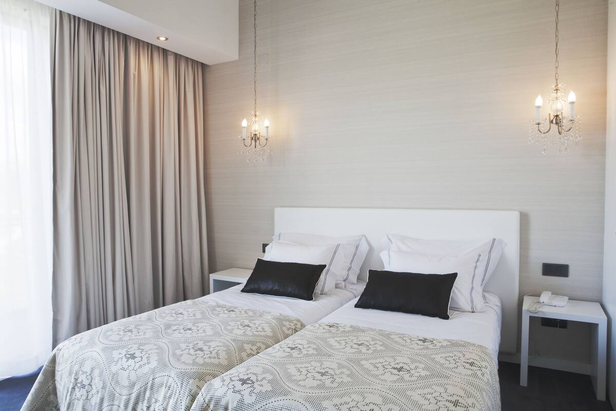 Una habitación de hotel con cama doble, dos mesitas de noche, un candelabro y un ventanal con cortinas.