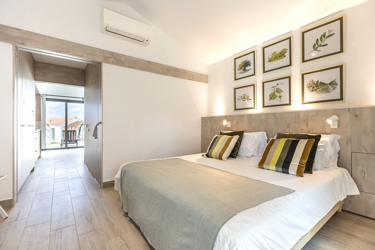 A modern bedroom with a large bed, a wooden headboard, and framed botanical artwork on the wall.