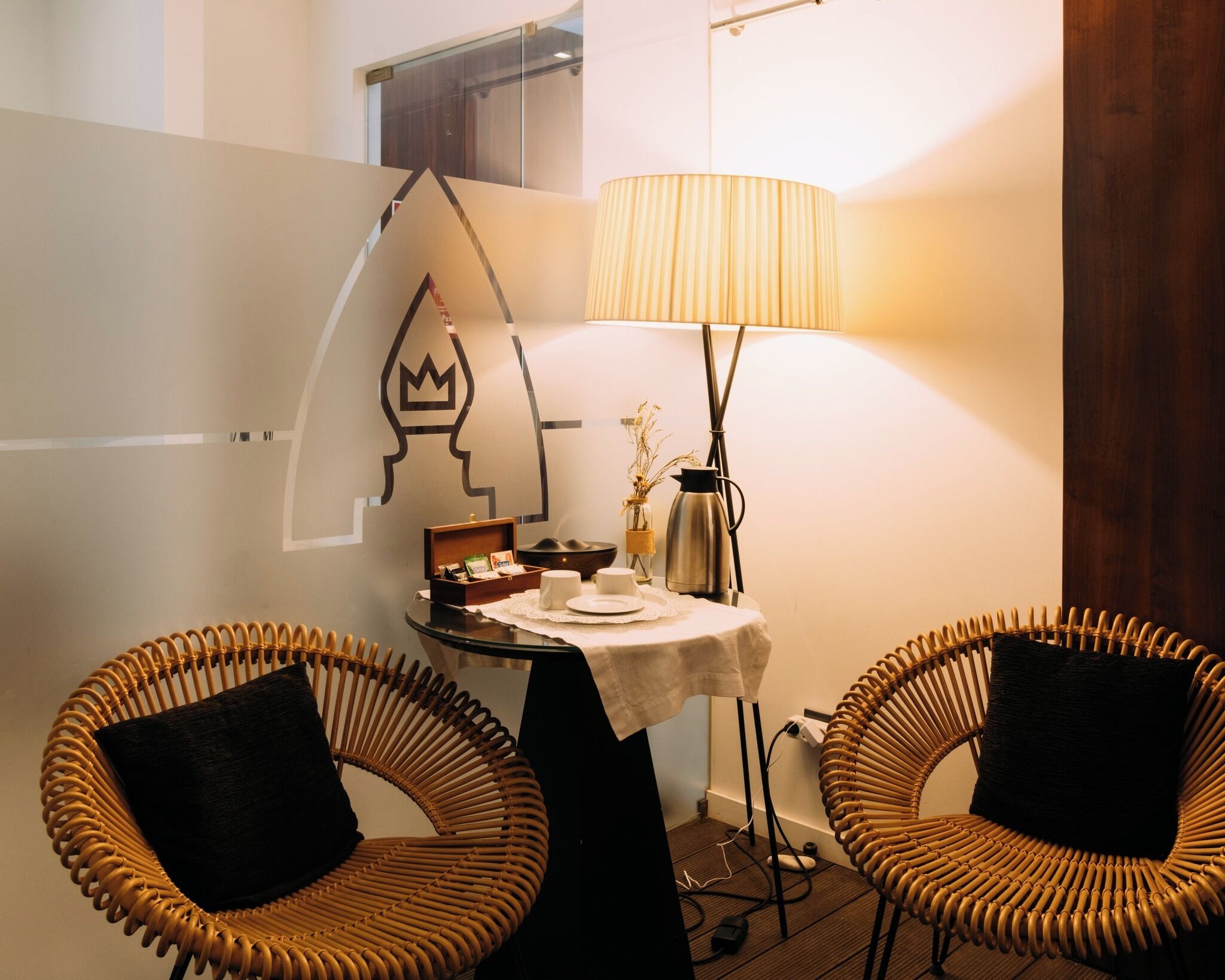 A small, cozy room with two wicker chairs, a table with a lamp, and a decorative wall piece.
